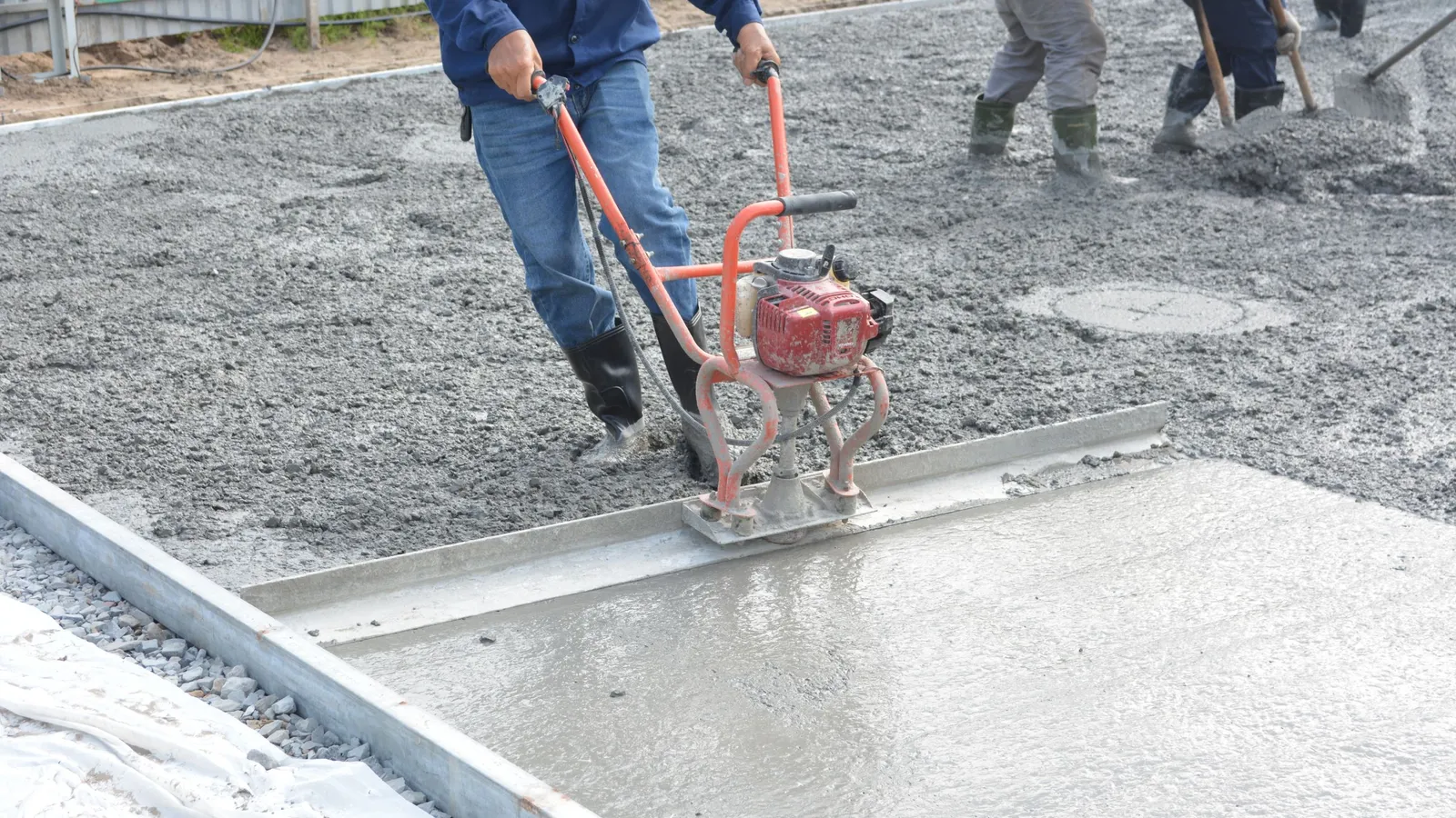 A worker levelling a freshly poured concrete slab with a power screed